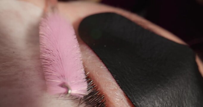 Macro probe tracking shot of eyelash brush applying mascara to closed eye with under eye pad in salon treatment room.