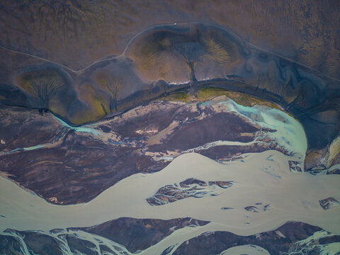 Aerial view of glacial river patterns flowing through dark volcanic terrain in Iceland.