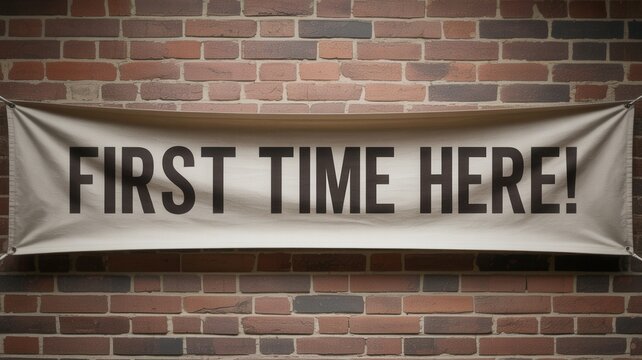 White fabric banner featuring bold black text first time here displayed prominently against a textured rustic dark red brick wall