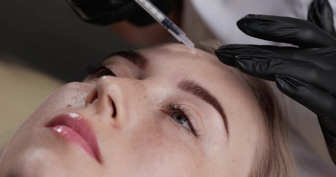 Handheld close up of woman receiving cosmetic injection to forehead in aesthetic clinic with subtle pan.