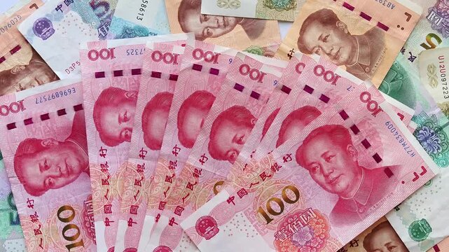 Hands count a stack of Chinese 100 yuan (CNY) banknotes and place it on top of bills of smaller denominations. Concept of savings, budgeting, wealth, income, banking and financial planning.