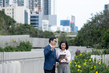 Fototapeta premium Asian business professionals walking and discussing work with digital tablet, representing teamwork, communication, collaboration, planning, technology, consulting, professional partnership.
