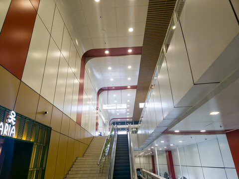 Interior view of a modern public building or transit station featuring an escalator, stairs, and contemporary illuminated ceilings