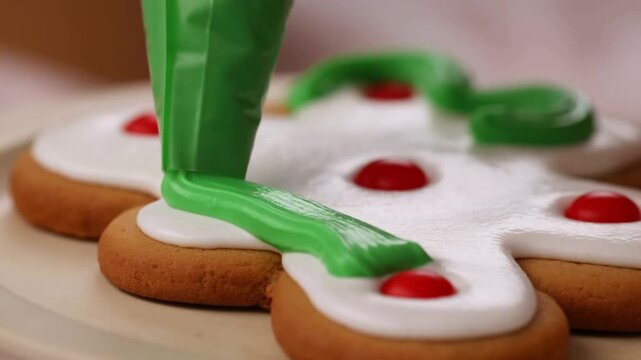 Slow motion tracking shot of piping bag applying green icing onto gingerbread cookie on wooden plate close up