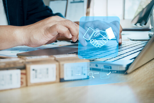 Businessman typing on laptop, office desk, parcel boxes and digital partnership handshake hologram graphic, concept of B2B e-commerce, procurement, supply chain management, online business agreement