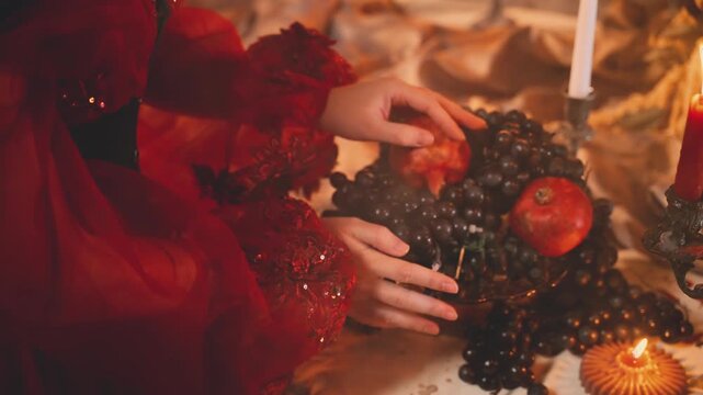 fairy tale woman queen hands touching ripe dark blue black grapes fresh fruits red garnet dish. in royal festive table medieval feast holiday decor. body part fantasy girl princess red dress old style