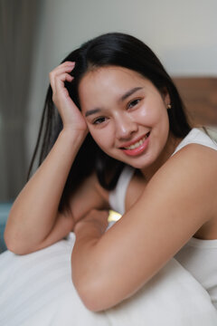 Young asian woman smiling and relaxing on a comfortable bed in the bedroom, having a peaceful and casual morning routine at home, feeling happy and natural