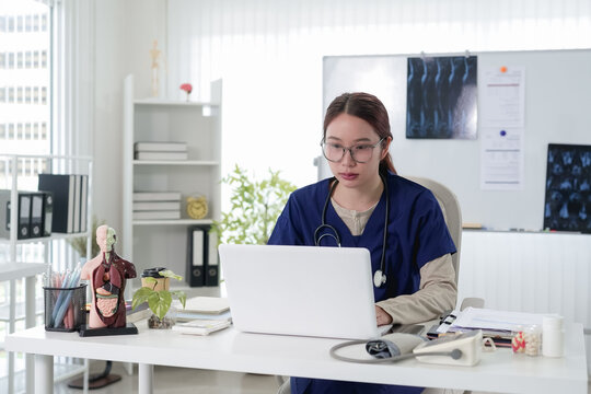 Young Asian female doctor wearing glasses using laptop for online medical consultation in modern clinic office