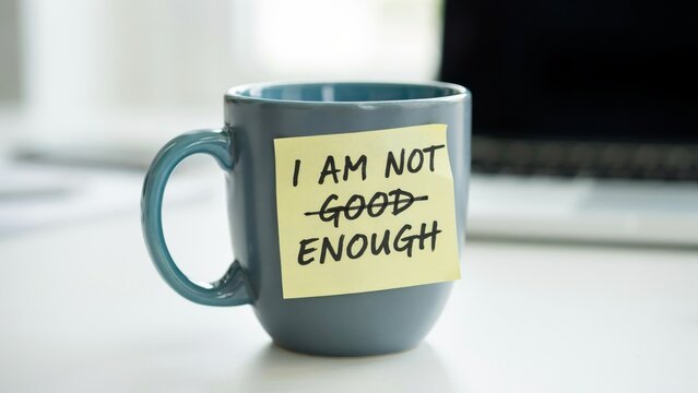 Self-affirmation message "I am good enough" on a sticky note attached to a coffee mug in an office setting.