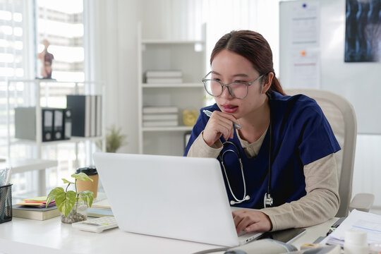 Young Asian female doctor wearing stethoscope conducting telemedicine consultation on laptop in modern clinic office