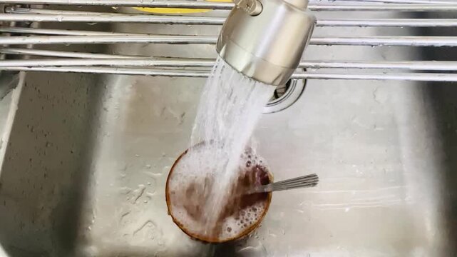 Running water flows from a kitchen faucet into a small bowl after eating, rinsing away remaining food residue as part of the dish cleaning proces.