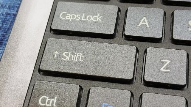 Close up macro top view of finger pressing laptop shift key button on modern laptop computer keyboard. Office professional work and data input concept. Closeup macro top view.