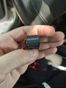 Hand holding a black car electrical relay showing model number and specifications