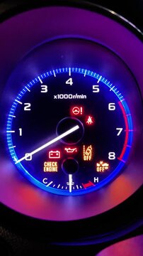 Car engine starting with a close up on the illuminated tachometer and glowing warning lights on the vehicle dashboard, indicating a system check before driving