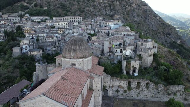 Aerial photography of an ancient Italian town featuring a Byzantine church dome. A drone camera flies over the historic stone rooftops and distinctive dome of the medieval church of Stilo in southern 