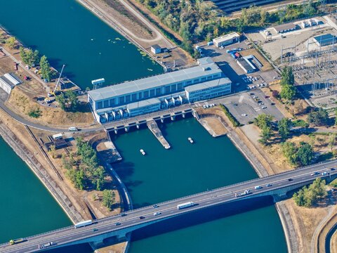 Aerial view of the Hombourg hydroelectric power plant and lock on the Grand Canal d'Alsace, featuring concrete infrastructure, blue water, and a bridge with traffic in Hombourg, Grand Est, France.