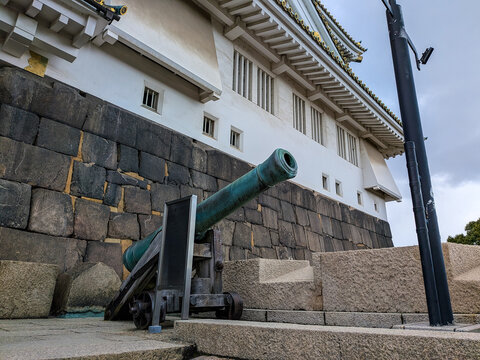 大阪城の強固な石垣と白い城壁を背に静かに佇む青銅製の大砲