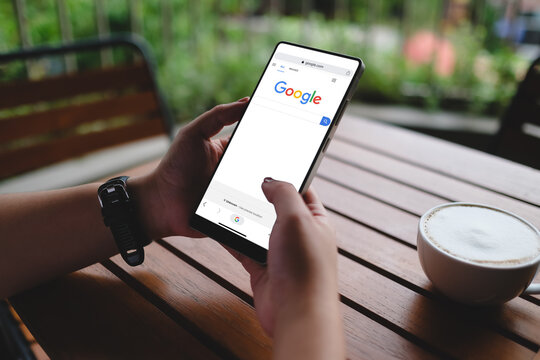 Bangkok, Thailand. August 16, 2026; Hands holding smartphone displaying Google search engine homepage interface while working in cafe.
