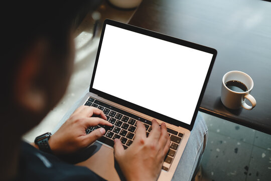 Over the shoulder view of person working on laptop with blank white screen mockup resting on lap.