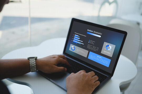 Close-up of hands typing on laptop displaying generic sales statistic dashboard with bar graphs and financial chart analytics.