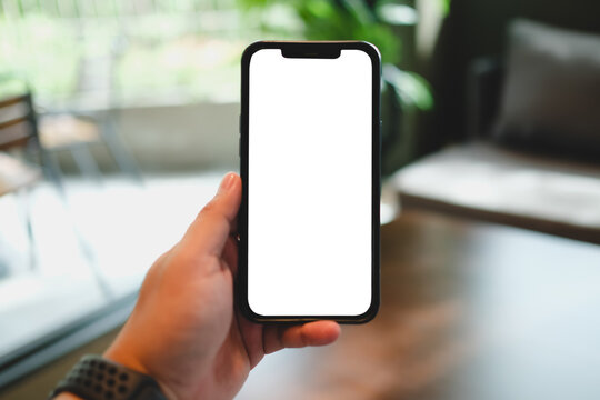Person hand holding vertical smartphone with empty blank white screen mockup for user interface showcase.