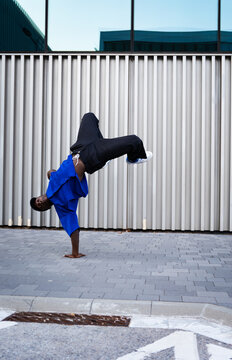 Breakdancing man balancing on one hand performing a freeze move on urban sidewalk against a modern building wall