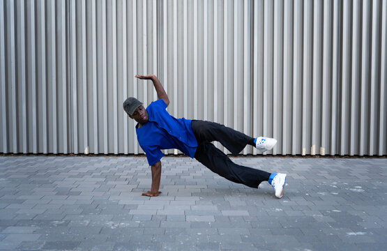 Young black man breakdancing outdoors, balancing on one hand with energy and skill, performing urban hip hop moves