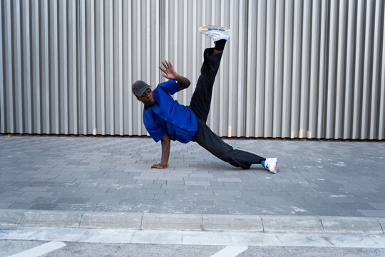 Breakdancer performing power moves on urban sidewalk, expressing athleticism, hip hop culture, and energetic street dance