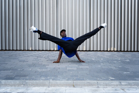 Breakdancing man performing power move on urban street, demonstrating strength, balance, and hip hop culture