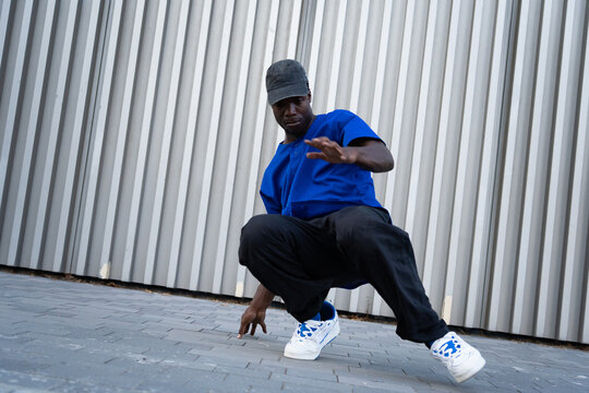 Black male breakdancer crouching in urban street style against a metallic wall, expressing hip hop culture and movement