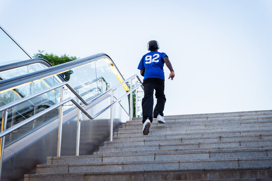 Young man jogging up urban stairs next to escalator, demonstrating fitness and determination for success
