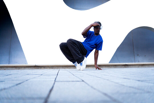 Young black man in headphones breakdancing on urban street, performing energetic hip hop dance move