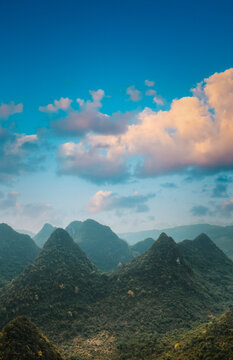 Scenic view of Yangshuo's distinctive cone shaped limestone mountains. Vibrant blue sky contrasts with green forested peaks. Classic Chinese landscape scenery showcasing natural beauty and tourism