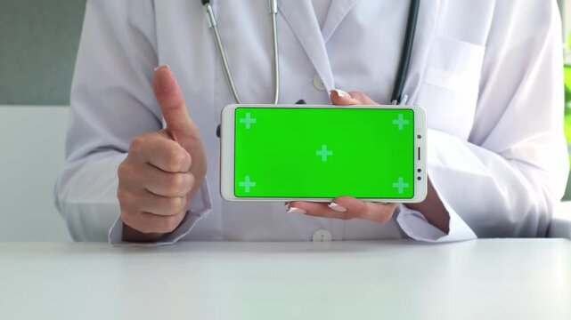 Woman doctor showing phone with green blank screen, presenting mockup for app or ad, pointing finger on it. Medicine, telemedicine and mobile technology