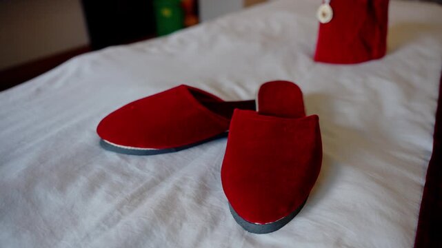 Red velvet wedding slippers in sharp focus with matching topi cap softly blurred in background on white bed low angle