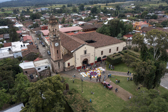 Aerial view of the Patamban floral rug in the courtyard of San Francisco de Asis church, surrounded by terracotta rooftops and lush greenery in Patamban, Michoacan, Mexico.