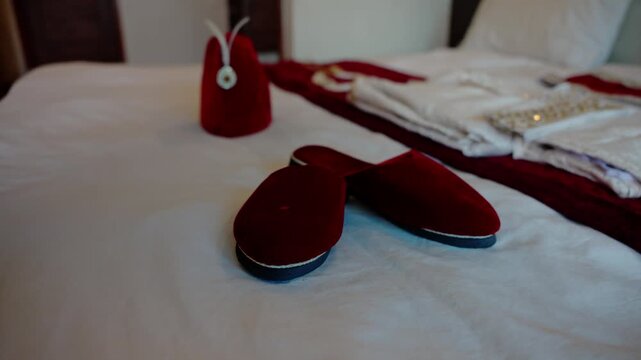 Groom slippers positioned in foreground with red velvet topi and folded embroidered kurta arranged softly out of focus behind them