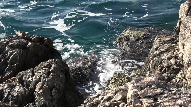 Kas, Turkey - 14 of February 2026: Waves splashing over rugged limestone coastal rocks 
