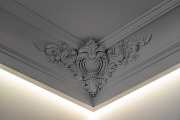 Elegant white ornamental ceiling corner with intricate classical plaster molding, decorative floral relief and integrated ambient LED lighting in a luxury interior © Viktor Brazhnikow