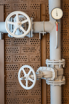 Industrial pipeline system with white control valves, pressure gauge and flanged pipe fittings mounted against textured brick wall