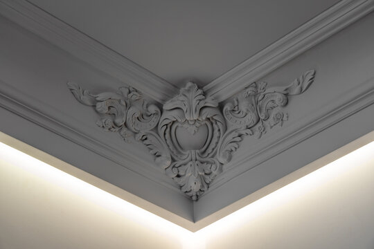 Elegant white ornamental ceiling corner with intricate classical plaster molding, decorative floral relief and integrated ambient LED lighting in a luxury interior