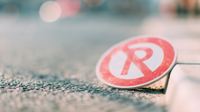 fallen no parking sign rests on textured asphalt beside concrete curb with soft bokeh background for advertising web design and urban mobility campaigns
