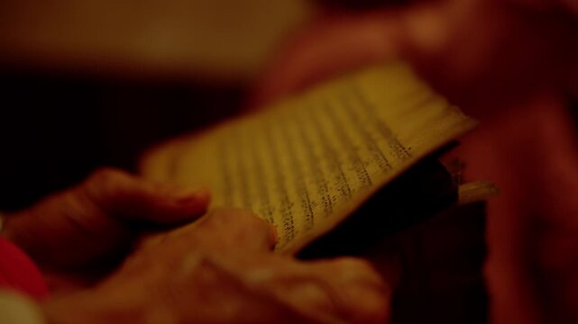 Single hand holding ancient handwritten manuscript at low angle with warm amber lighting and softly blurred figure in the background