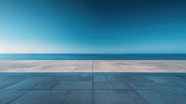 Minimal seaside promenade with large tiled stone terrace, calm blue ocean and wide clear sky conveying tranquil solitude and open horizon