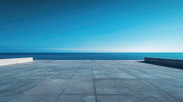 Empty tiled concrete terrace overlooking a calm blue sea and clear sky, framed by low concrete walls on both sides, minimalist tranquil coastal horizon