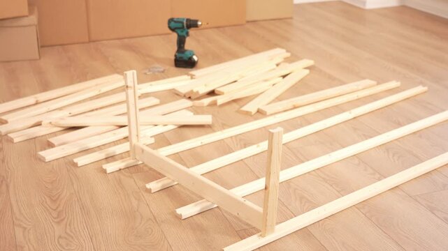 Wooden planks lay on a light floor. Some form a frame structure. Green drill sits nearby. Room has wooden cabinets in background. Ideal for DIY woodworking projects. Great for home improvement videos