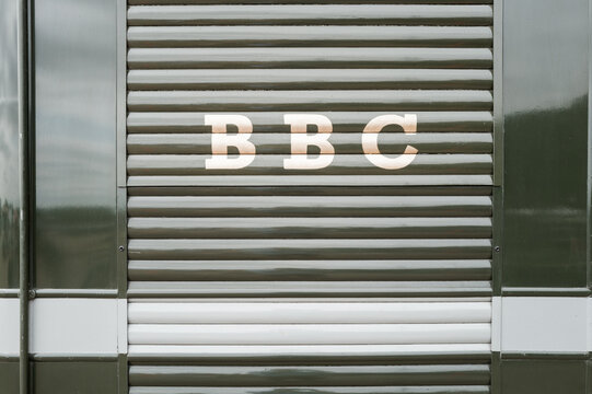 Famous BBC Radio and television corporation logo seen in gold lettering at the rear of a 1940s era outside broadcasting truck. The roll up door contains broadcasting equipment.