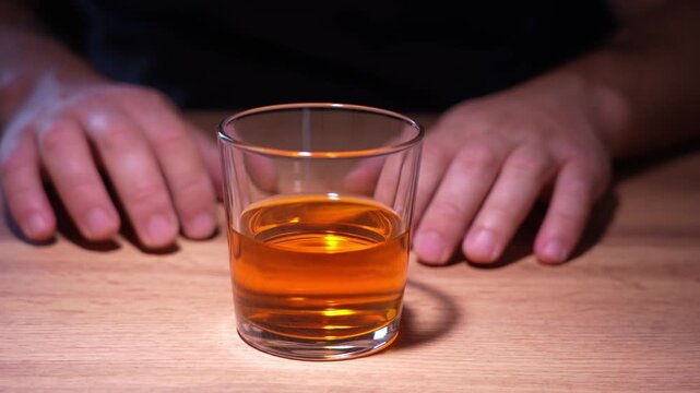 A man in front of a glass of alcohol struggles with the desire to drink an alcoholic drink. Alcoholism addiction is an irresistible desire to drink alcohol. Concept