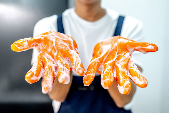 Male housekeeper showing hands with orange rubber glove full with soap suds after cleaning in the kitchen. Cleaning for hygiene. Wet work household chores