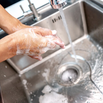 Washing hands with soap and running water from faucet on stainless steel kitchen sink. Hand hygiene after doing housework chores
